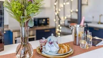 A dining table with a vase of flowers, a teapot, a plate of pastries, and a pitcher of champagne.