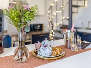 Una mesa de comedor con un jarrón de flores, una tetera, un plato de pasteles y una jarra de champán.