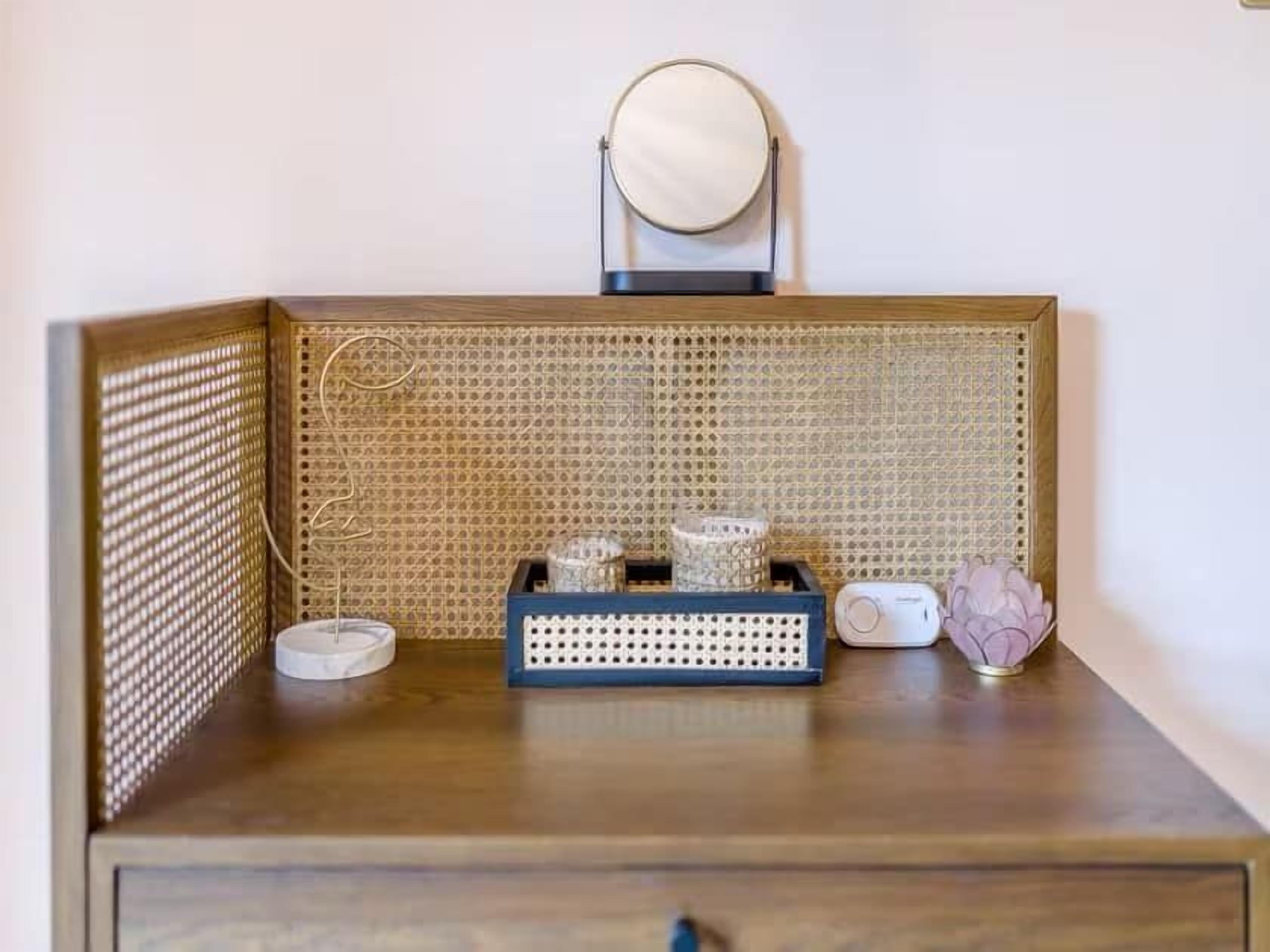 A wooden bedside table with a woven basket, a small white speaker, and a decorative item on a white wall.