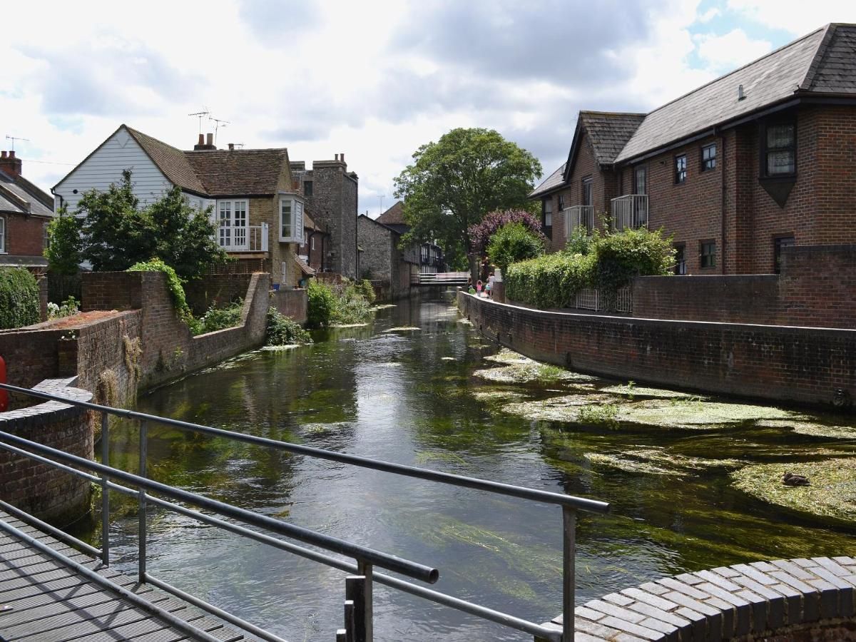 Un canal bordé de bâtiments en briques de chaque côté, une rambarde métallique et un arbre en arrière-plan.