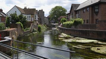 Un canal bordé de bâtiments en briques de chaque côté, une rambarde métallique et un arbre en arrière-plan.