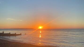 A beach with a sunset, calm water, and a rocky shoreline.