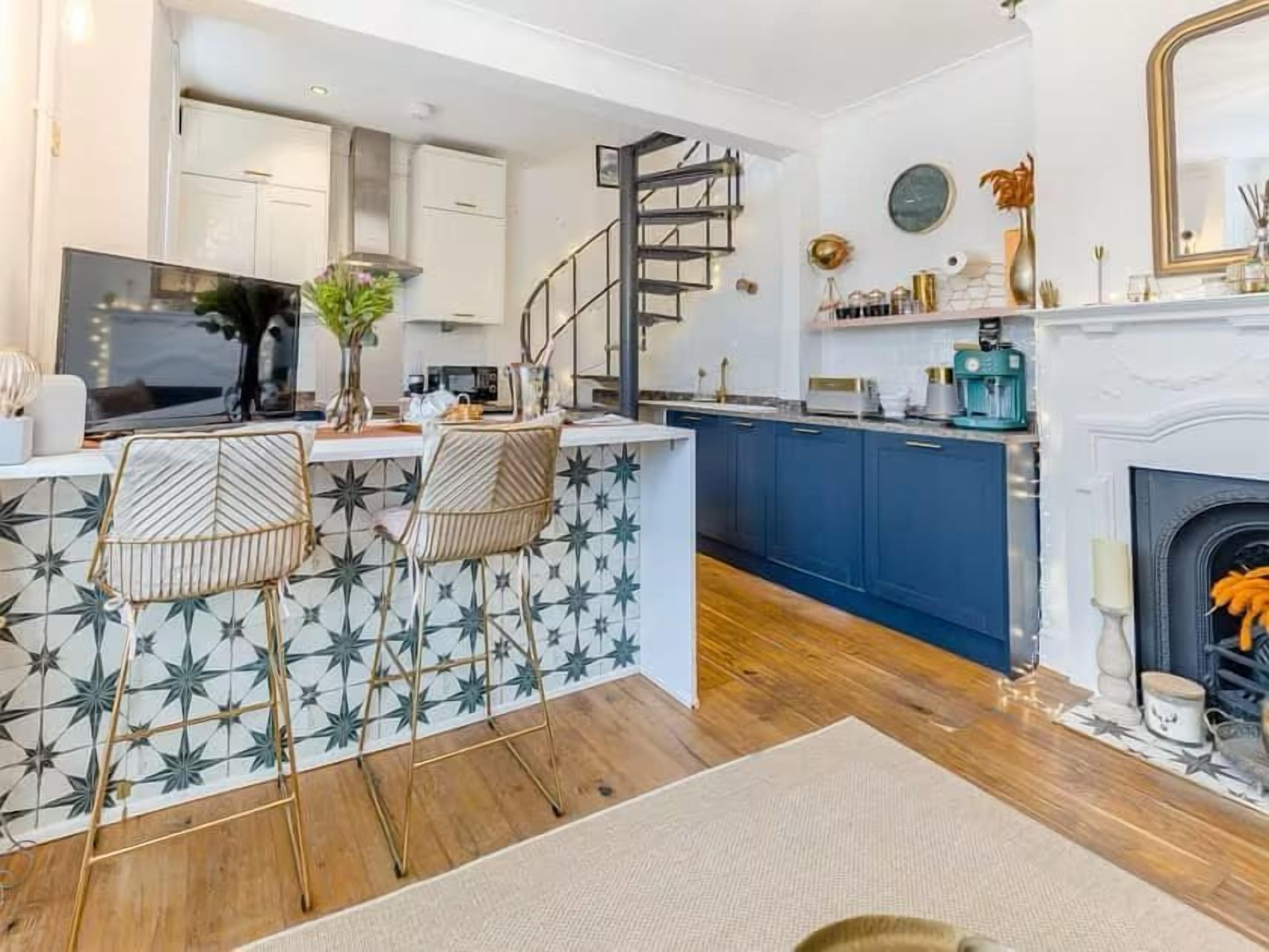 A modern kitchen with a central island, bar stools, a staircase, and a fireplace.