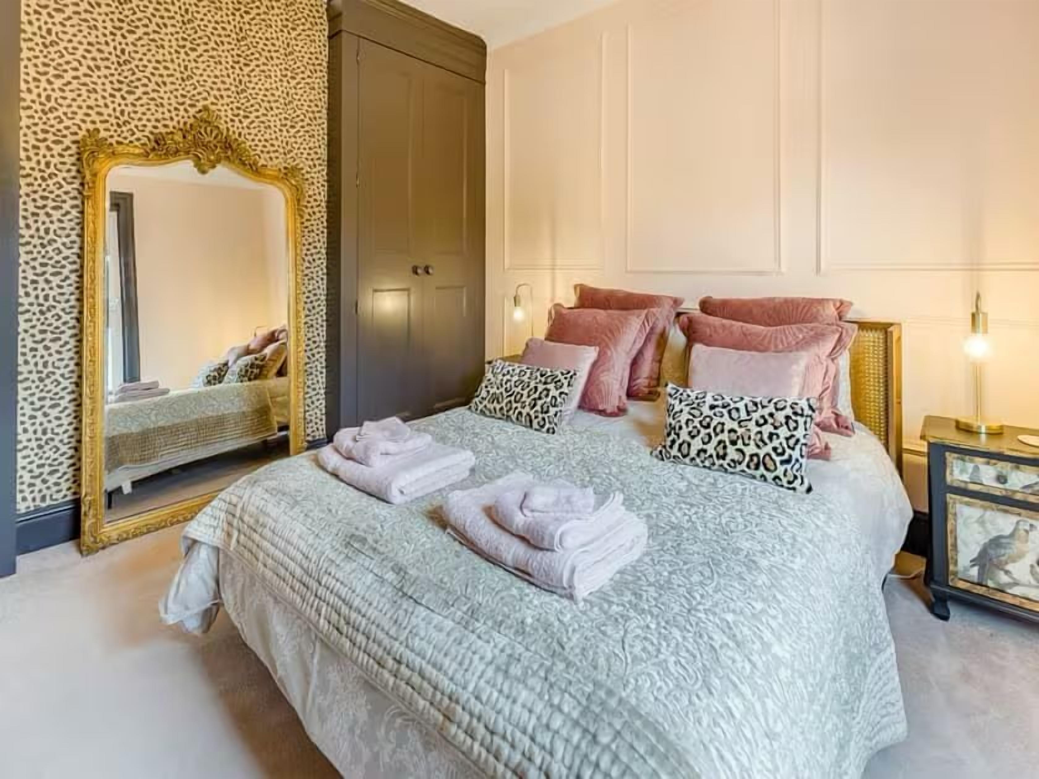 Ein ordentlich bezogenes Bett mit Kissen und gefalteten Handtüchern, ein großer Spiegel und ein Kleiderschrank in einem gut beleuchteten Zimmer.