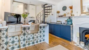 A modern kitchen with a central island, blue cabinets, and a spiral staircase. - Railway Cottage - Stylish & Central Oasis in Whitstable (Whitstable)