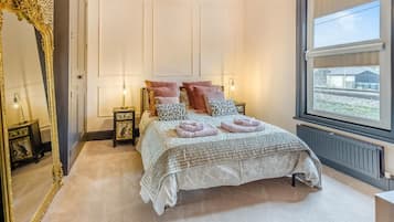 A bedroom with a large bed, a mirror, bedside tables, and a window.