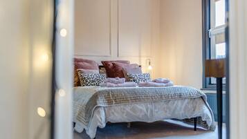 A bedroom with a bed, pillows, a bedside lamp, and a window.