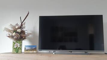 A flat-screen TV on a wooden TV stand with a decorative vase and a small framed picture beside it.