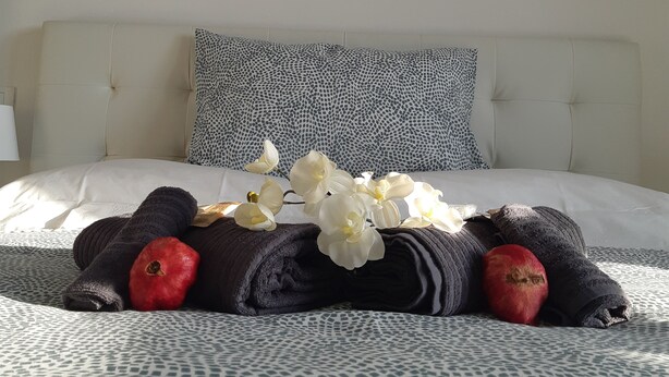 A neatly made bed with a patterned bedspread, a decorative pillow, and a bouquet of white flowers. - L'Aurora (Novi Ligure)