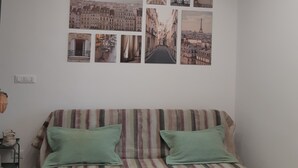 A living room with a striped sofa, a wall-mounted light fixture, and a series of cityscape photographs. - L'Aurora (Novi Ligure)