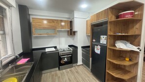 Uma cozinha compacta com armários de madeira, geladeira preta e forno embutido.