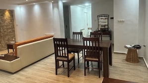 Uma área de refeições moderna com mesa e cadeiras de madeira, sofá branco e parede de pedra decorativa.