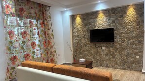 Sala de estar com um sofá, televisão fixada em parede de pedra e cortina florida.