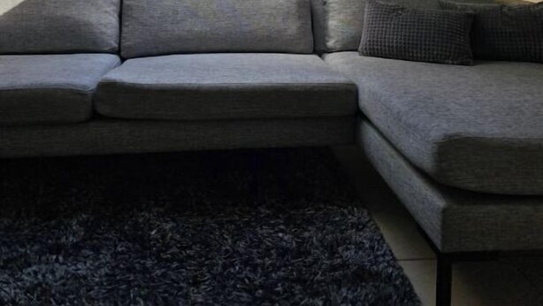Una habitación con tragaluces, un sofá seccional gris y una alfombra oscura.