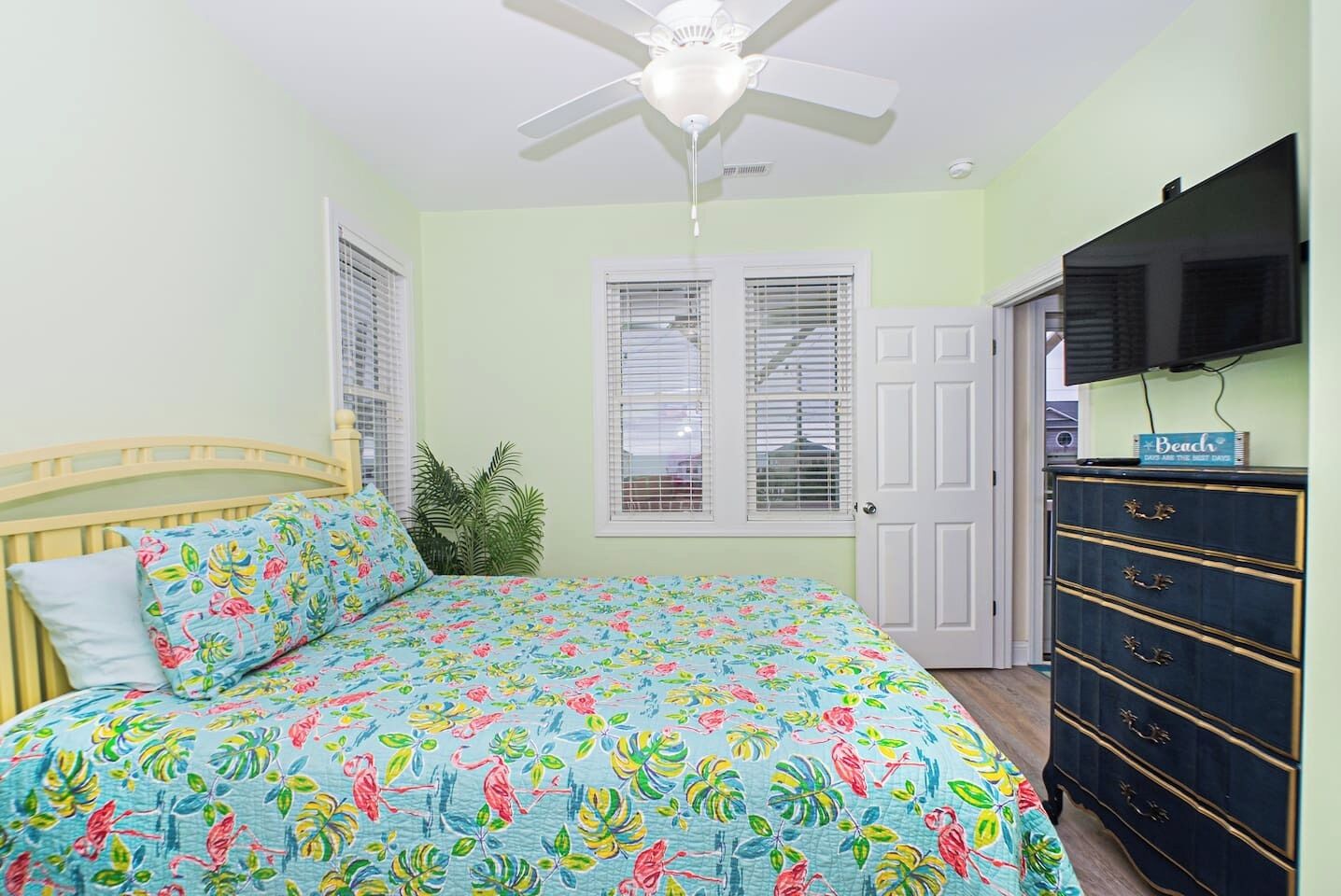 A bedroom with a bed, a ceiling fan, a dresser, and a door.