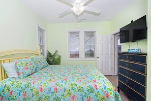 A bedroom with a bed, a ceiling fan, a dresser, and a door.