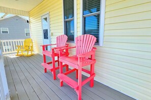 A porch with two Adirondack chairs and a bench.