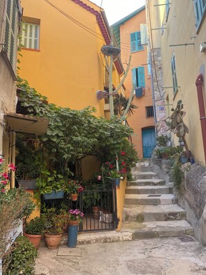 Un vicolo stretto con un edificio giallo, una scala e piante in vaso.