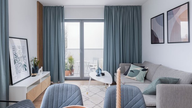 A modern living room with a sofa, a dining table, and a balcony with a view. - RentPlanet - Apartament Prandoty (Kraków)