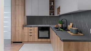 A modern kitchen with wooden cabinets, a black countertop, and a built-in dishwasher. - RentPlanet - Apartament Prandoty (Kraków)