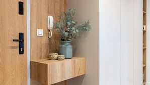 A modern hallway with a wooden door, a small bench, a shelf with a vase and plant, and a phone on the wall. - RentPlanet - Apartament Prandoty (Kraków)