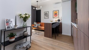 A modern kitchen with wooden cabinets, a dining area with a bar stool, and a living space with a sofa and a coffee table. - RentPlanet - Apartament Prandoty (Kraków)