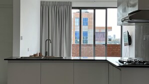 Una cocina moderna con estufa integrada, una ventana con cortinas y vistas a un edificio de ladrillo.