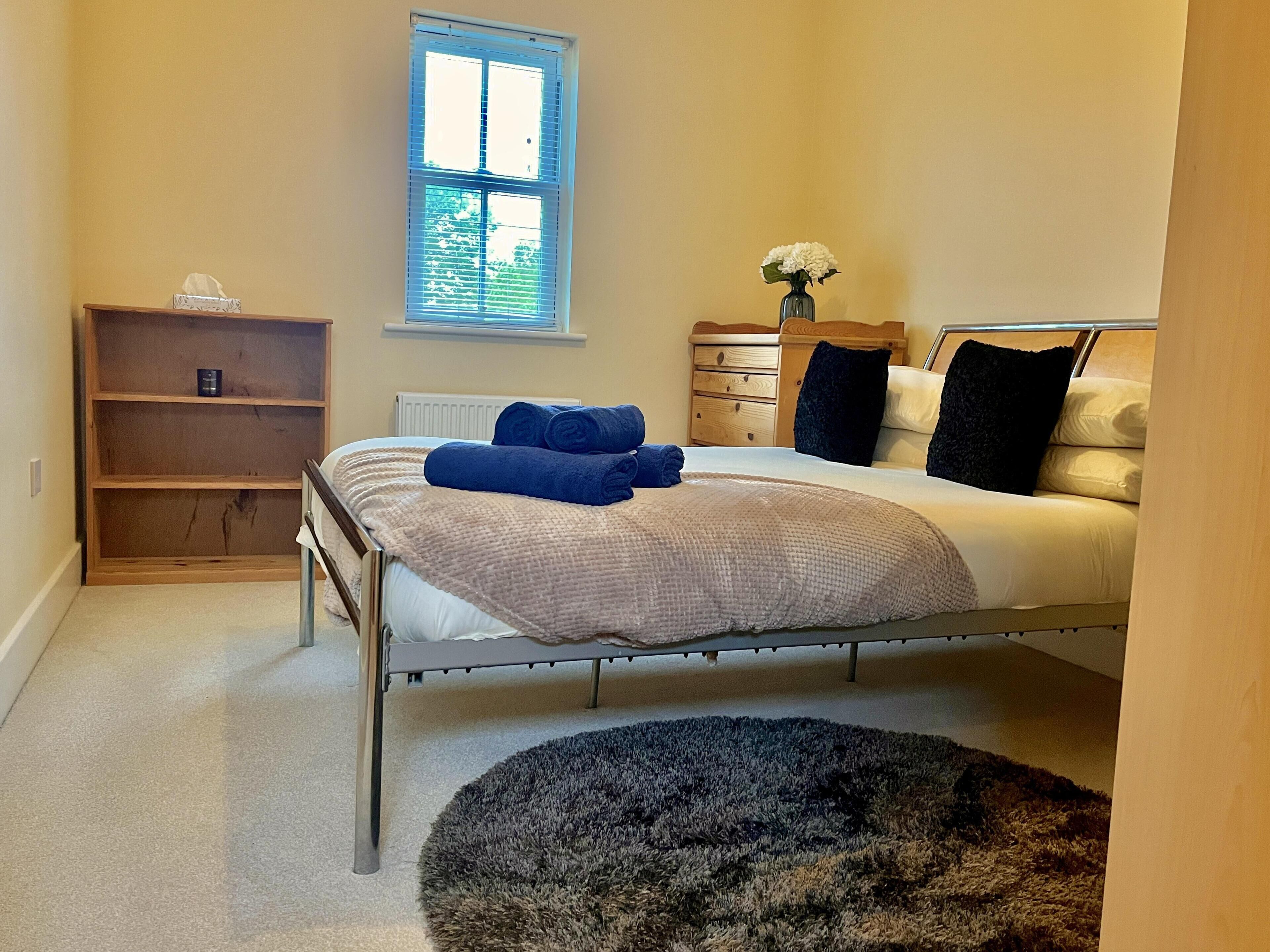 A bedroom with a bed, a nightstand, a window, a shelf, and a rug.