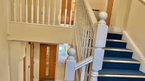 Un escalier avec des balustrades blanches et des marches recouvertes d’une moquette bleue, menant à un palier.