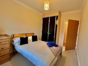 A neatly made bed with white and black pillows, a wooden headboard, and a bedside table with a lamp. - Captivating 1-bed Apartment in Cambridge (Cambridge)