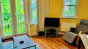 Un salon avec un téléviseur, un canapé et une table. De grandes portes-fenêtres coulissantes donnent sur un jardin.