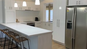 Eine moderne Küche mit weißen Schränken, einem Edelstahlkühlschrank und einer langen Kochinsel mit Barhocker.