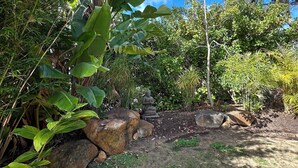 Ein Garten mit Buddha-Statue, großen Felsen und üppiger Vegetation.