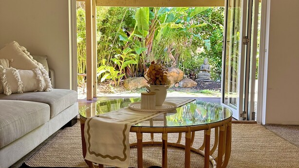 Ein Zimmer mit Glastisch, einer Couch und Blick auf einen Garten durch eine Glastür.
