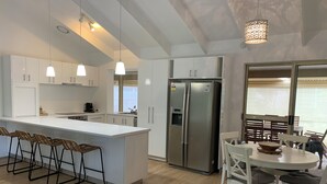 Eine moderne Küche mit weißen Schränken, einer zentralen Kochinsel mit Barhocker, einem Edelstahlkühlschrank und einem Essbereich mit rundem Tisch und Stühlen.