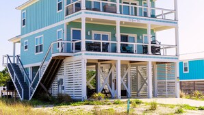Una casa de playa de varios niveles con un balcón, una escalera y un espacio cubierto.