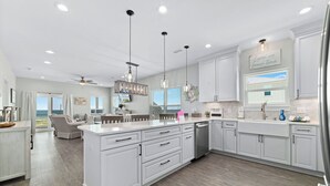 Una cocina amplia con muebles blancos, una isla grande e iluminación colgante.