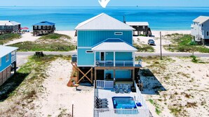 Una propiedad frente a la playa con un edificio central azul, una piscina y varias construcciones más pequeñas.