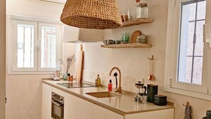 Una cucina con isola centrale, una lampada a sospensione in fibra naturale e mensole integrate sopra il piano di lavoro.