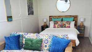 Ein Schlafzimmer mit einem Bett, einem runden Spiegel, einem Wandbild und einem gemusterten Sofa.