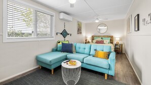 Ein modernes Wohnzimmer mit einem petrolfarbenen Ecksofa, einem runden Couchtisch und einem Deckenventilator.
