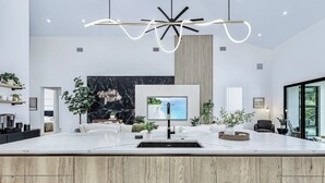 Een moderne keuken met een marmeren aanrechtblad, een inbouwspoelbak en een groot eiland. Er is een televisie aan de muur bevestigd, een houten kast onder het eiland en een hanglamp erboven.