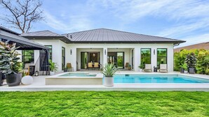 Een modern huis met een zwembad, een overdekt terras en een verzorgd gazon.