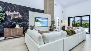 Een moderne woonkamer met een grote bank, een flatscreen televisie en een marmeren muur met een 'Naples Park' bordje.