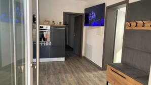 Una cocina moderna con horno y microondas integrados, un banco de madera con ganchos y un televisor de pantalla plana montado en la pared.