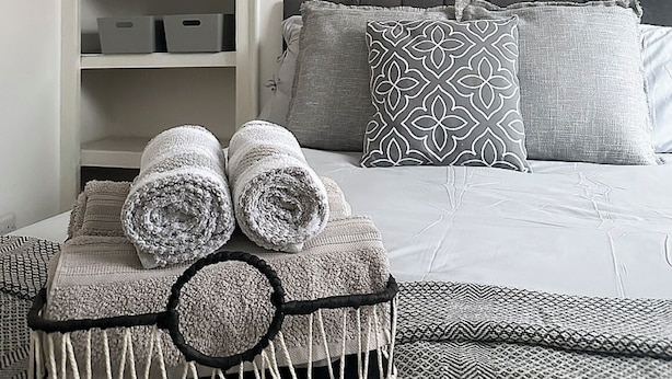 Una camera da letto ordinata con un letto, cuscini e un comodino con asciugamani.