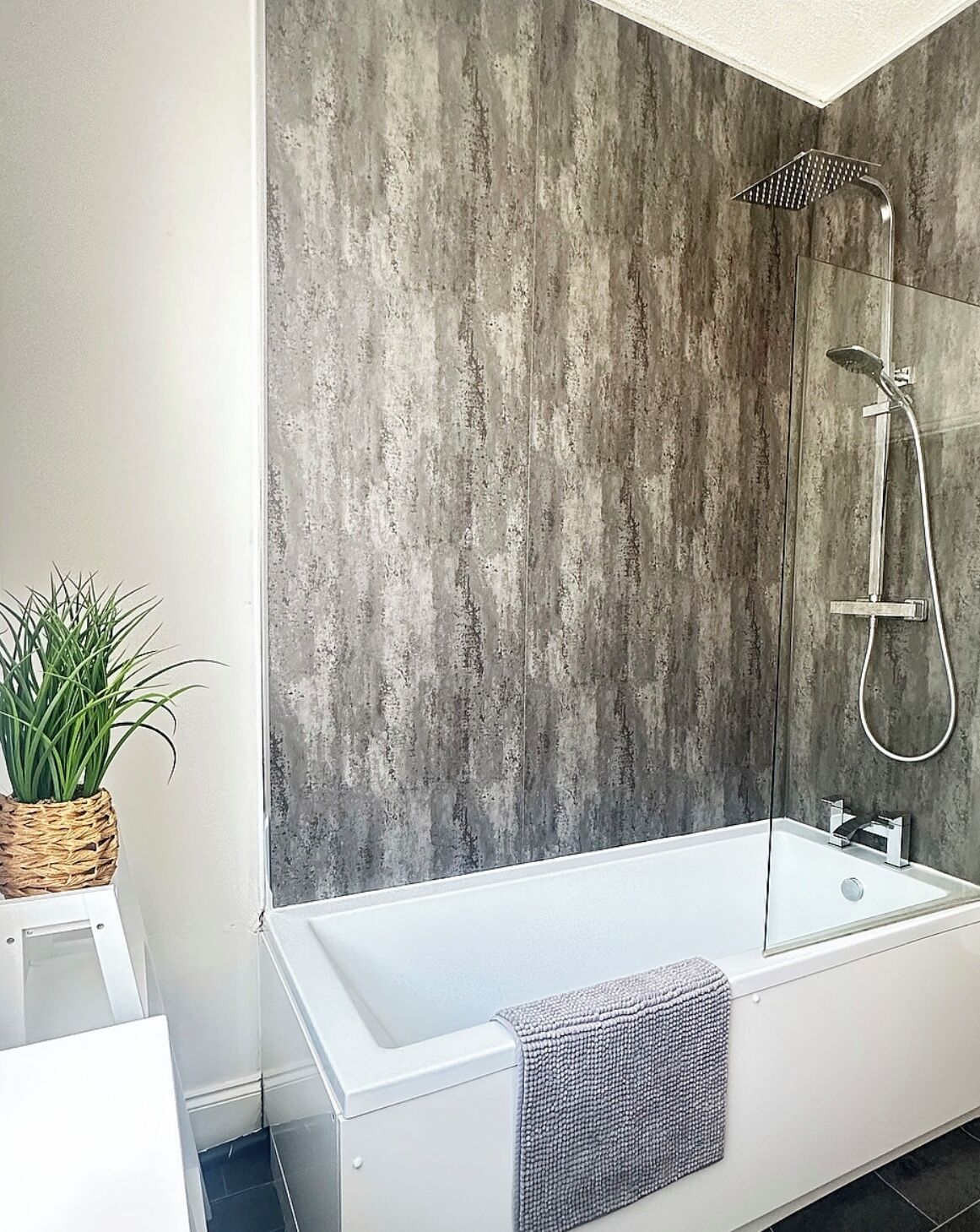 Une salle de bain moderne dotée d’une grande baignoire, d’une douche avec un pommeau de douche à effet pluie et d’un mur à texture.