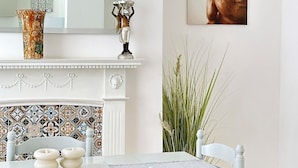 Un'area pranzo con tavolo bianco, sedie, zoccolo di piastrelle decorate, uno specchio, una statua di Buddha e un vaso.
