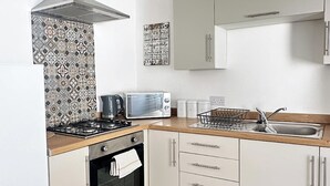 Una cucina compatta con fornello a gas, forno a microonde, bollitore ed un lavello. Sono presenti pensili e una parete rivestita in piastrelle.