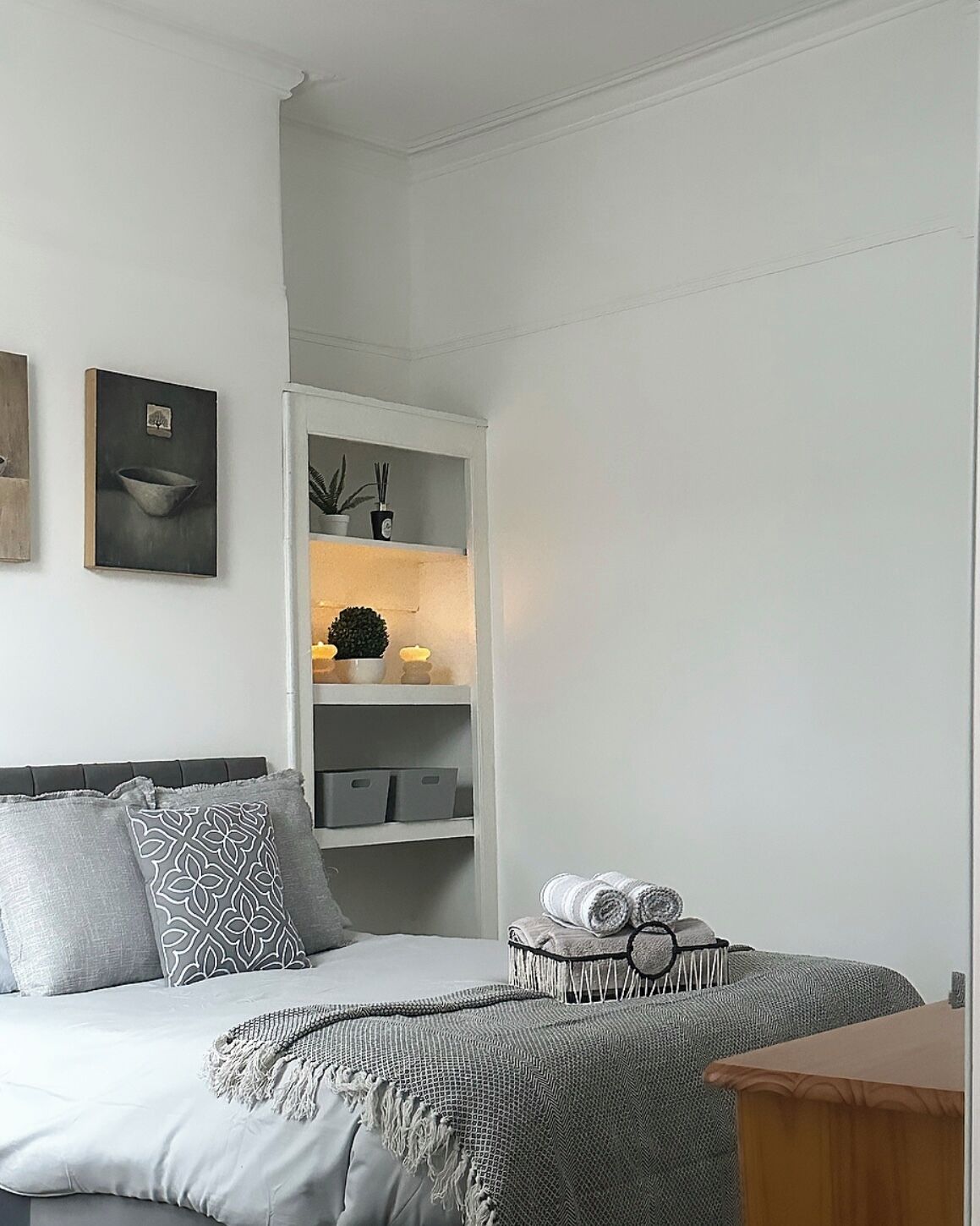 Una camera da letto con un letto, un comodino, una mensola con oggetti decorativi e un quadro appeso al muro.
